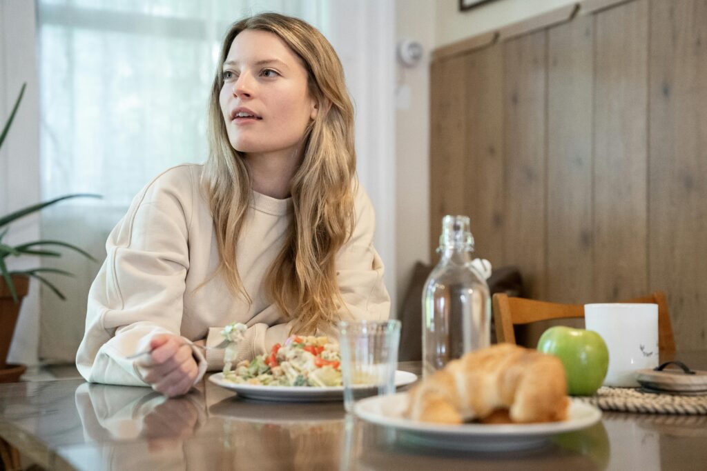 A Woman in Beige Long Sleeve Shirt Eating at the Table